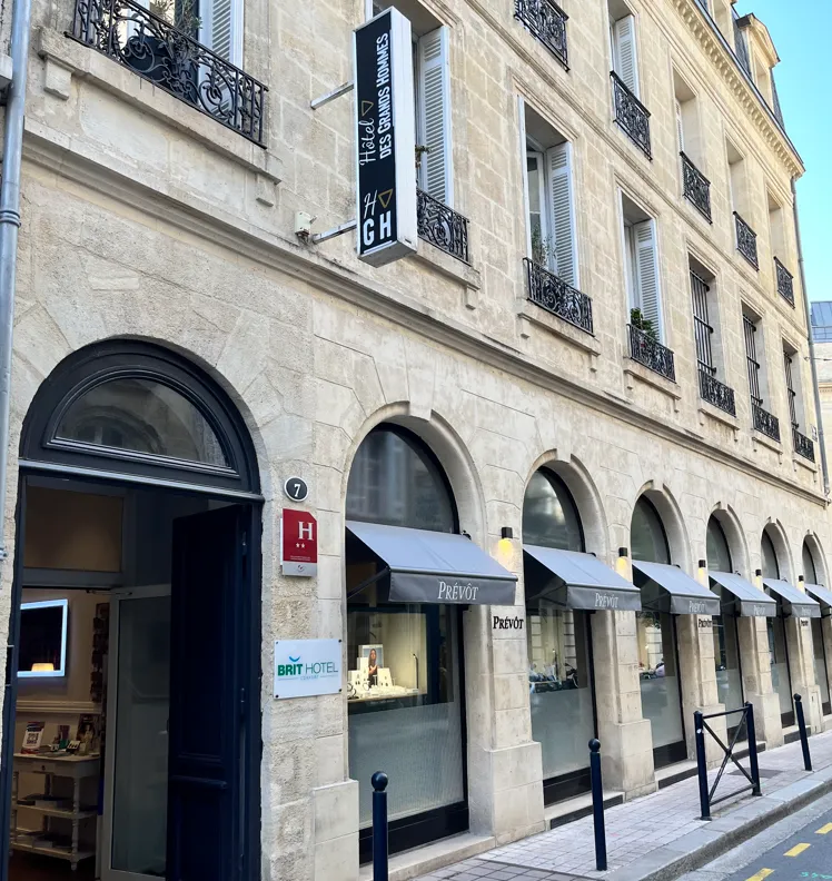 Facade of the Hôtel des Grands Hommes in Bordeaux, a stone building with ground-floor arcades, wrought-iron balconies on upper floors, and a Brit Hotel sign.