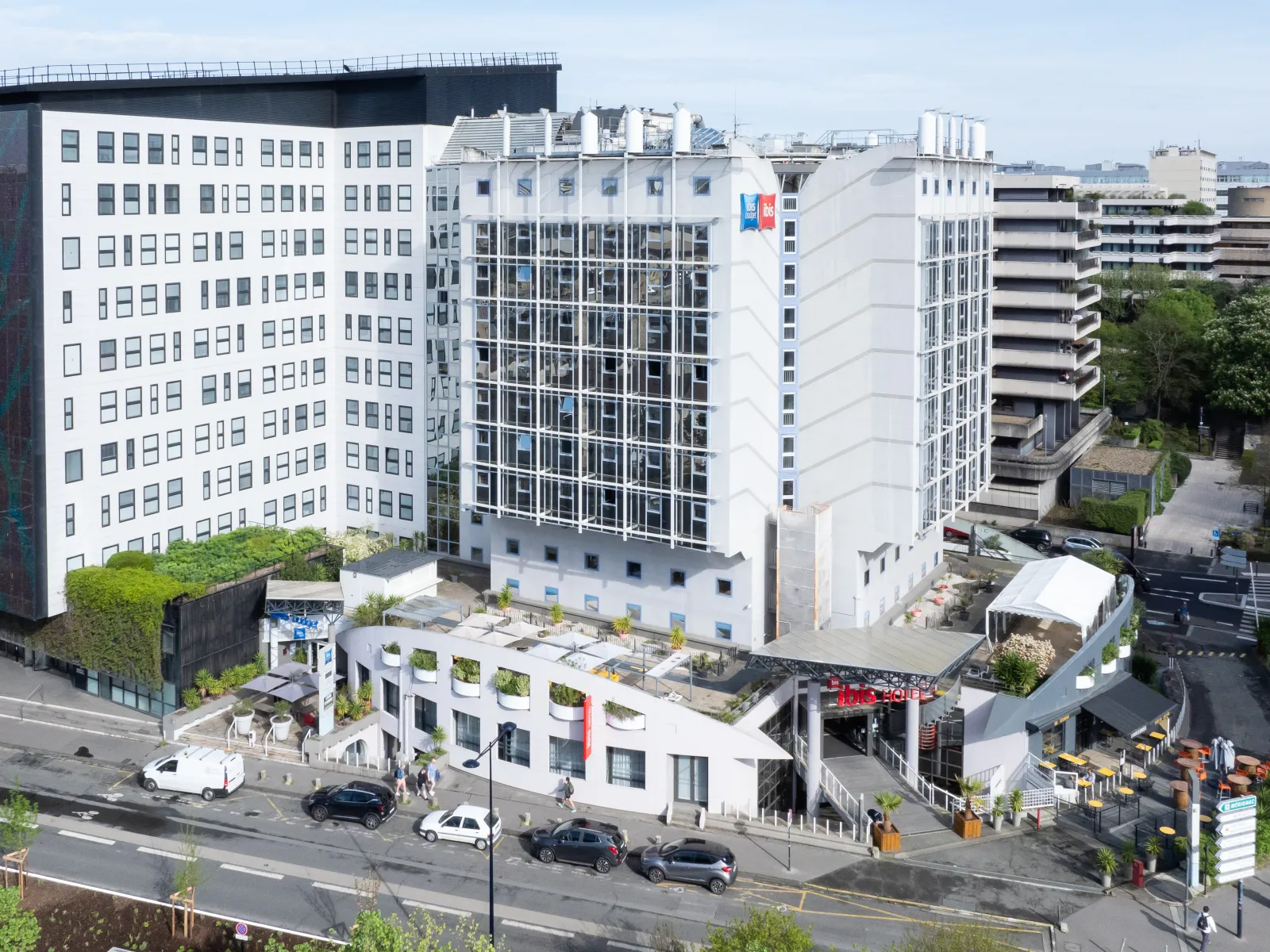Aerial view of Ibis Bordeaux Centre Mériadeck hotel featuring modern white buildings surrounded by residential and commercial towers, with green spaces and parked vehicles below.