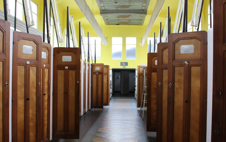Corridor of Bordeaux municipal swimming pool Les Bains featuring wooden changing cabins on both sides, bright yellow ceiling and access doors at the end