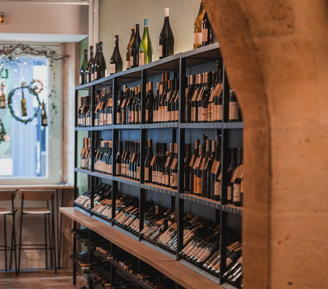 Wine display in ComplanTerra wine shop in Bordeaux, featuring bottles arranged on multiple black shelves with additional bottles displayed on top.