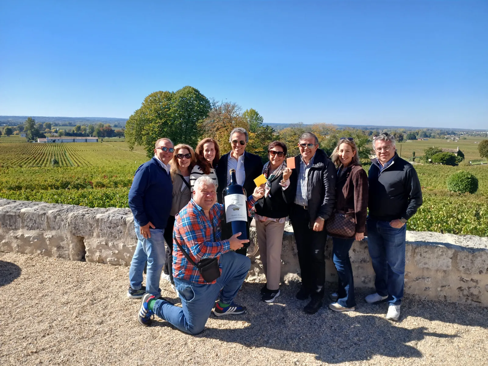Group of tourists posing with a wine bottle overlooking Bordeaux vineyards and rural landscape