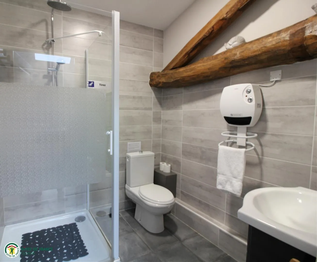 Modern bathroom featuring an Italian shower, white toilet, round sink, exposed wooden beam on ceiling, light gray tile and bathroom accessories