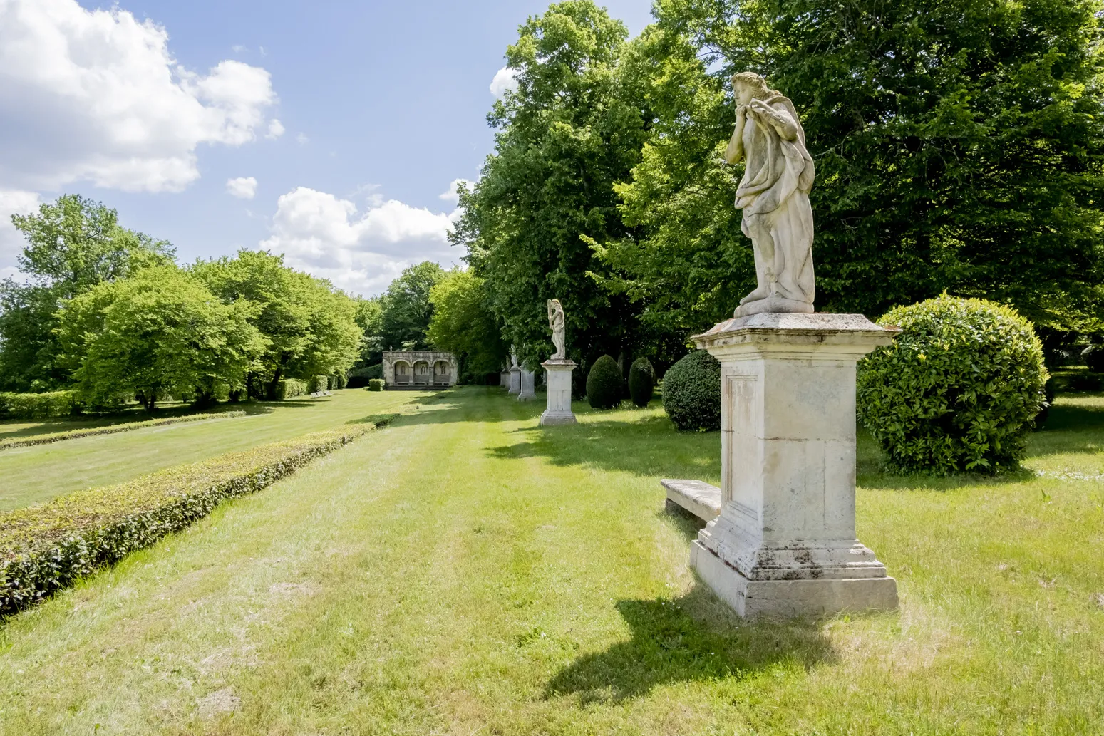 Tree-lined garden path at Château de Malle in Bordeaux featuring classical statues on pedestals and manicured lawns