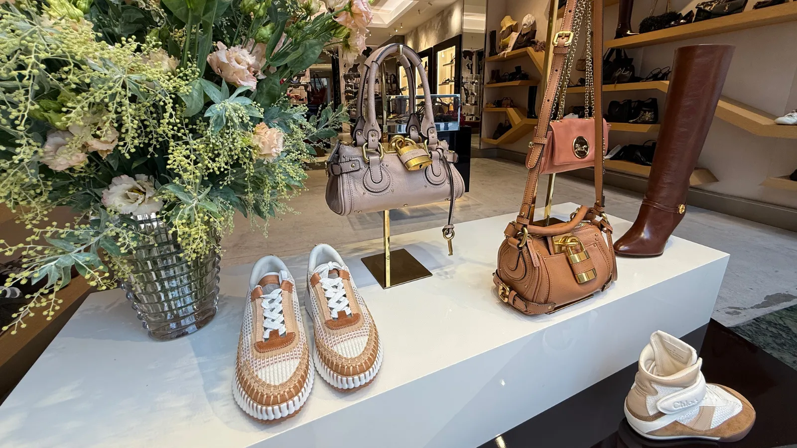 Luxury boutique window display in Bordeaux featuring leather shoes, handbags and boots, decorated with green plants and pink flowers