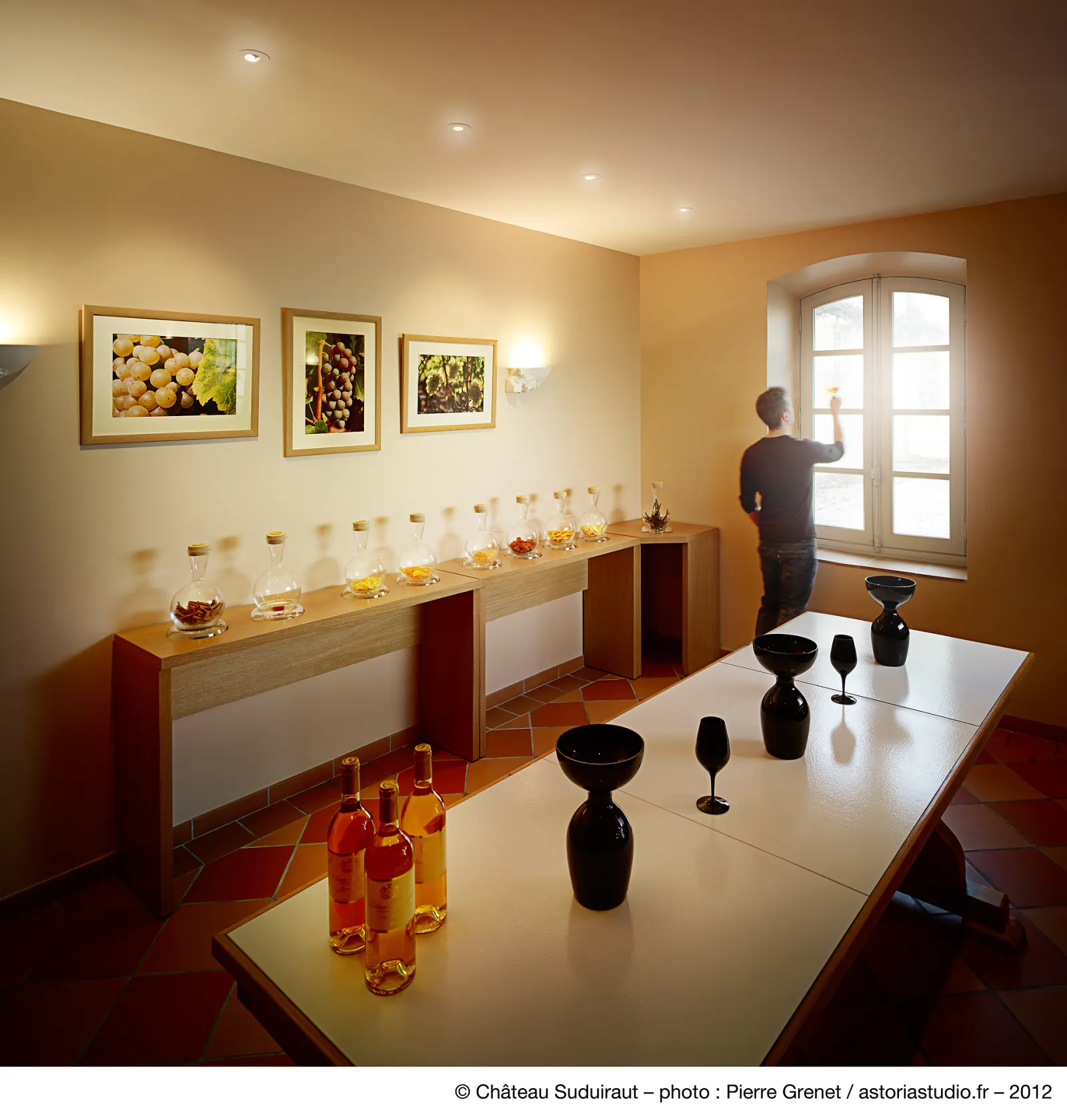 Wine tasting room at Château Suduiraut in Bordeaux featuring a white table, rosé wine bottles, black glasses, grape vineyard artwork, and wine samples in containers