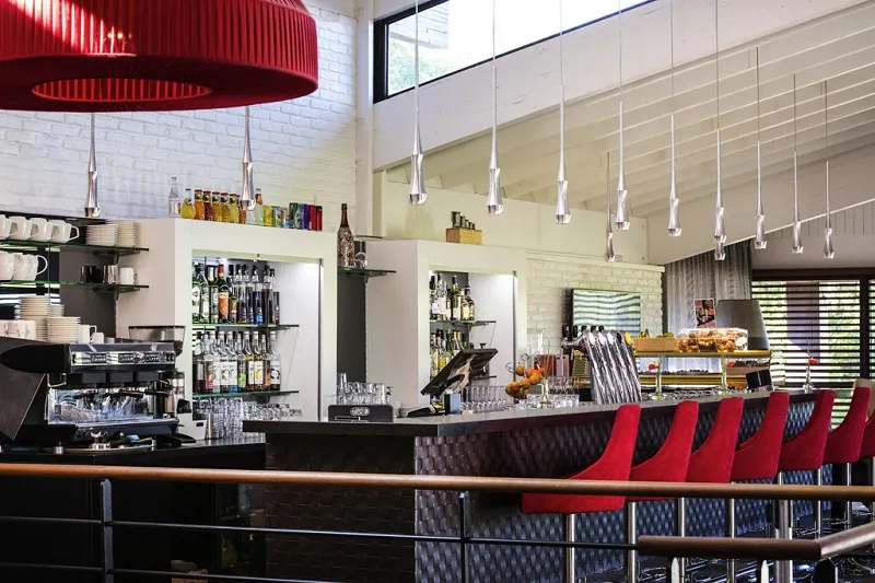 Modern bar interior featuring a black counter, red and blue stools, pendant lights, circular red ceiling, and bottle shelves in Bordeaux.