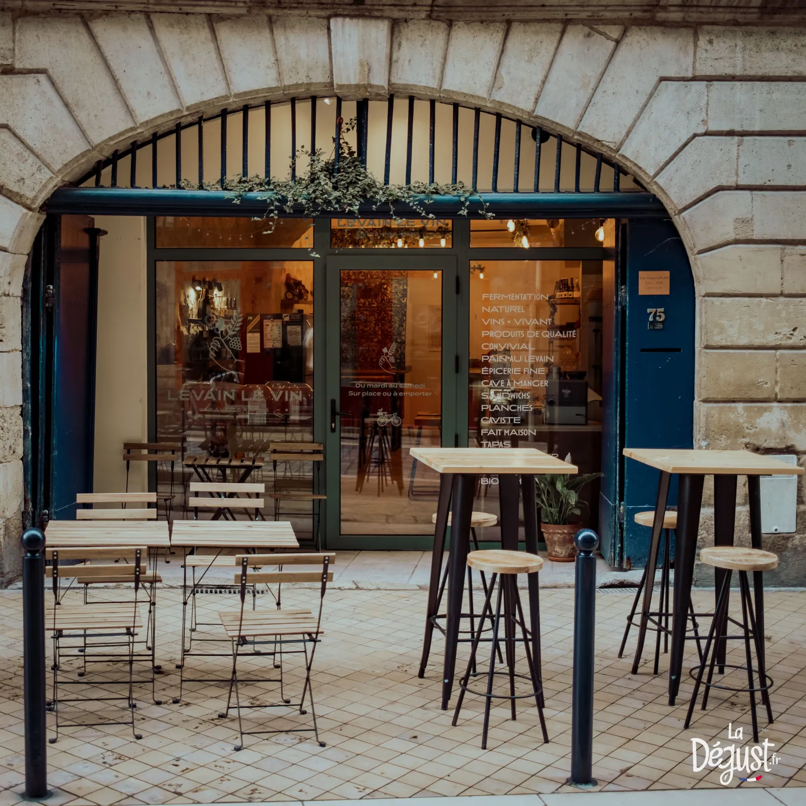 Storefront of Levain Le Vin restaurant in Bordeaux featuring blue facade, large windows and outdoor terrace with high tables and bar stools