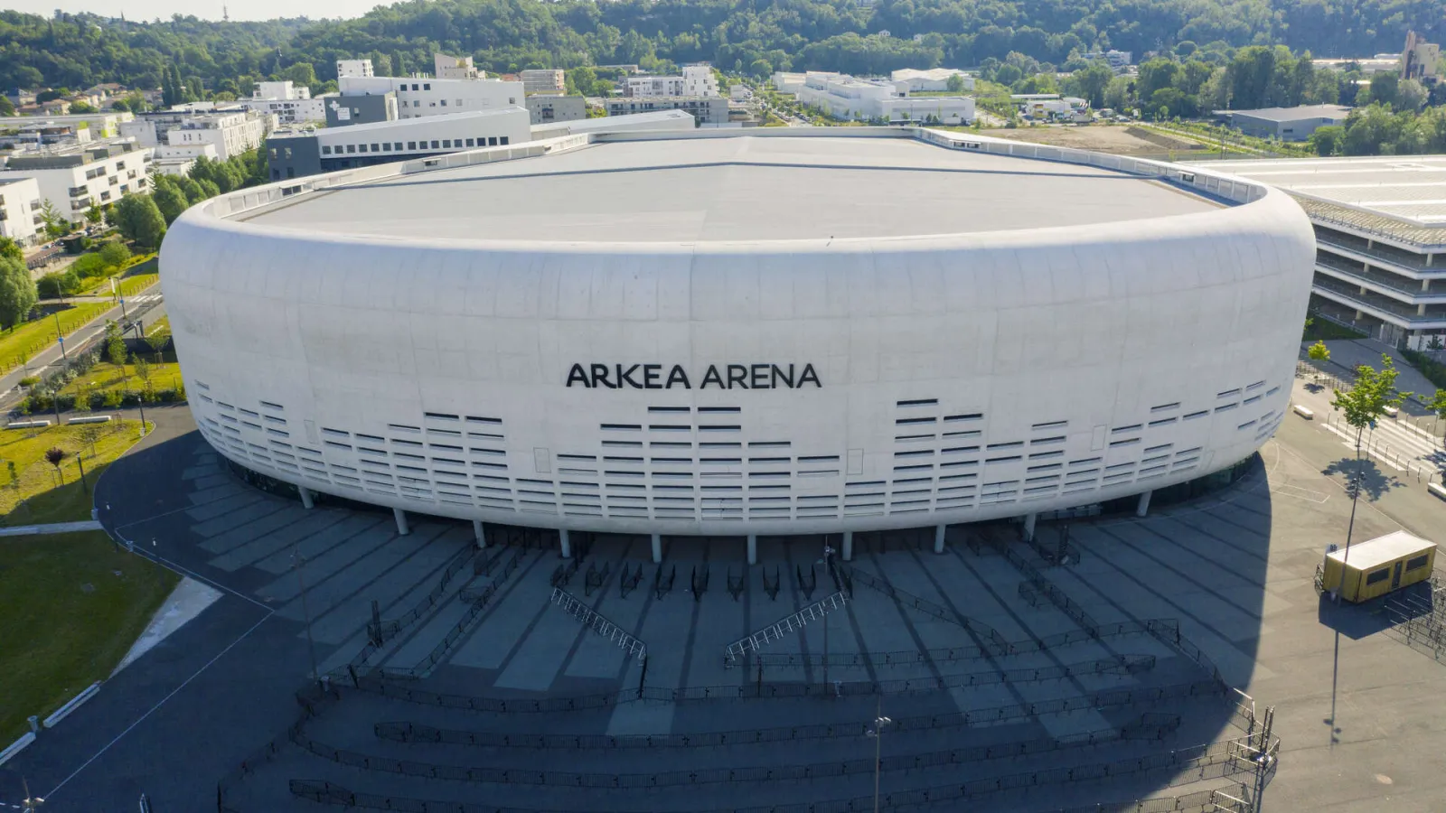 Aerial view of Arkea Arena, a modern white and grey rounded arena located in Floirac near Bordeaux, with parking areas and access plaza in the foreground.