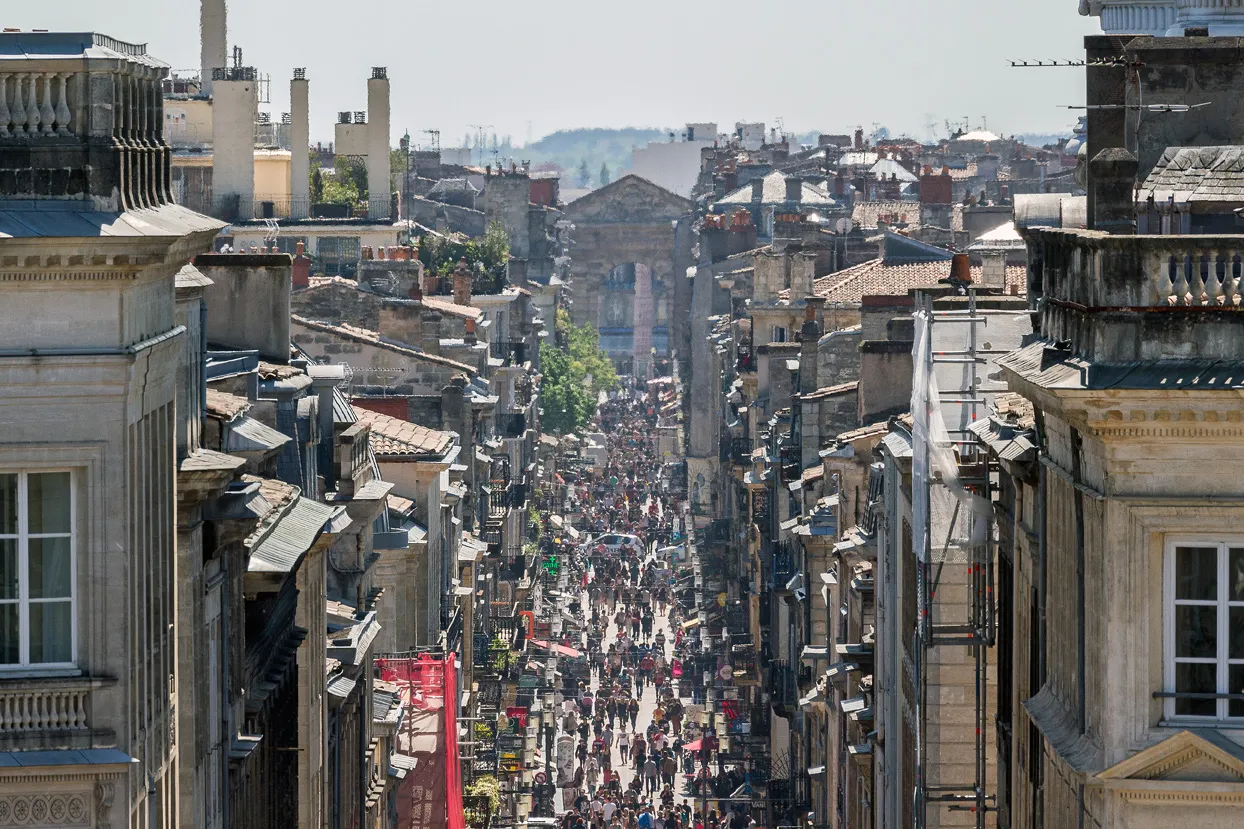 Panoramic view of Sainte-Catherine Street in Bordeaux, a long pedestrian street lined with historic stone buildings, crowded with people and shops.
