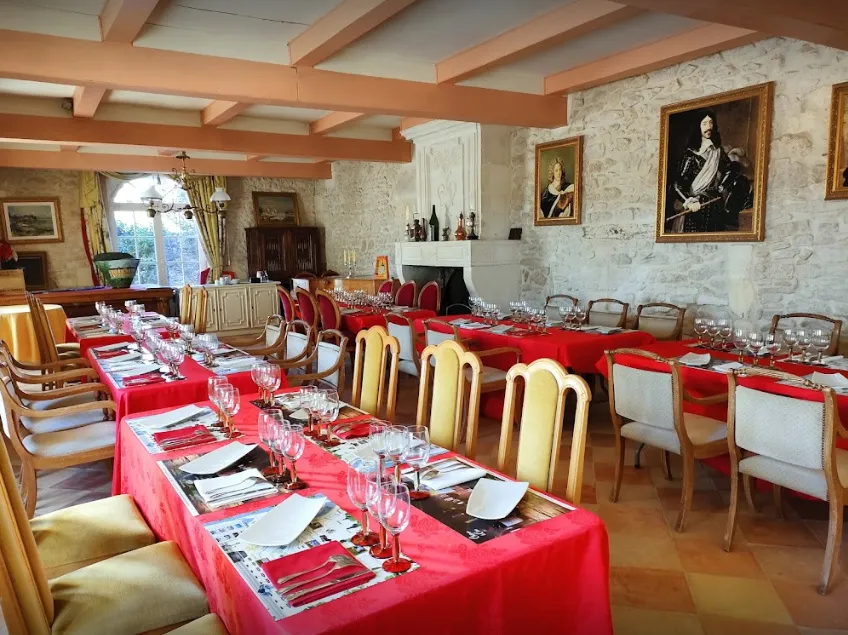 Elegant dining hall at Château Marquis de Vauban in Bordeaux featuring two tables draped in bright red tablecloths, gold and white chairs, place settings, crystal glassware, exposed wooden beams on the ceiling and historical portraits on the walls