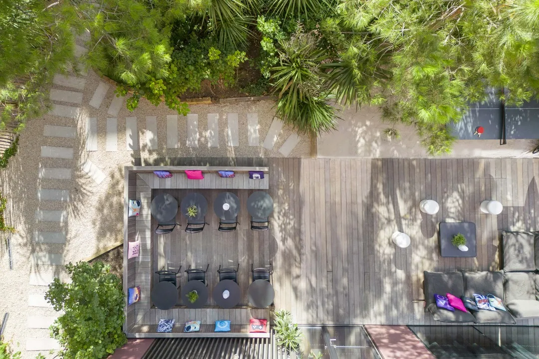 Overhead view of a modern rooftop terrace at Moxy Bordeaux hotel featuring lounge chairs, low tables, lush greenery and shaded relaxation areas
