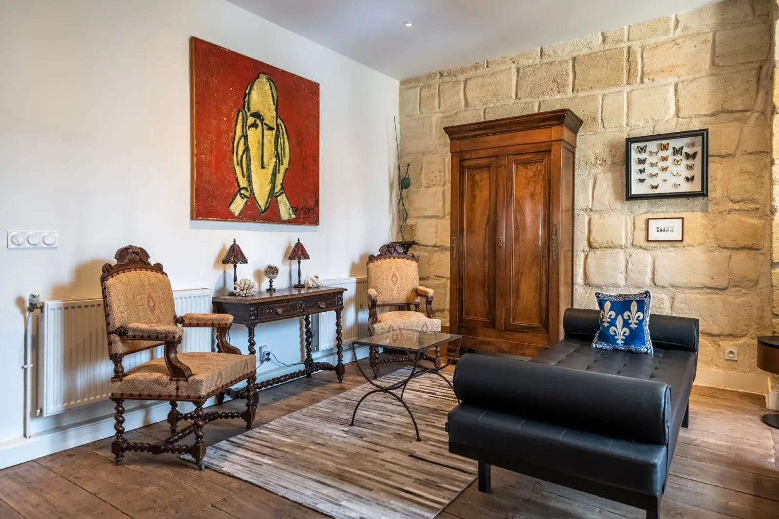 Elegant living room at La Monnoye in Bordeaux featuring antique furniture, exposed stone walls, red painting with stylized banana, and a blend of classic and contemporary styles.