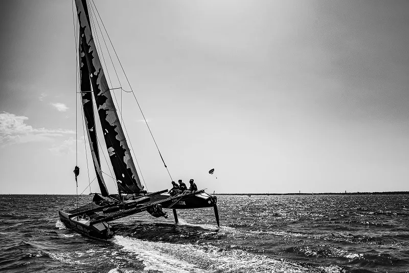 Black and white photograph of a sailing catamaran with crew members on board, sailing on open water near Bordeaux.