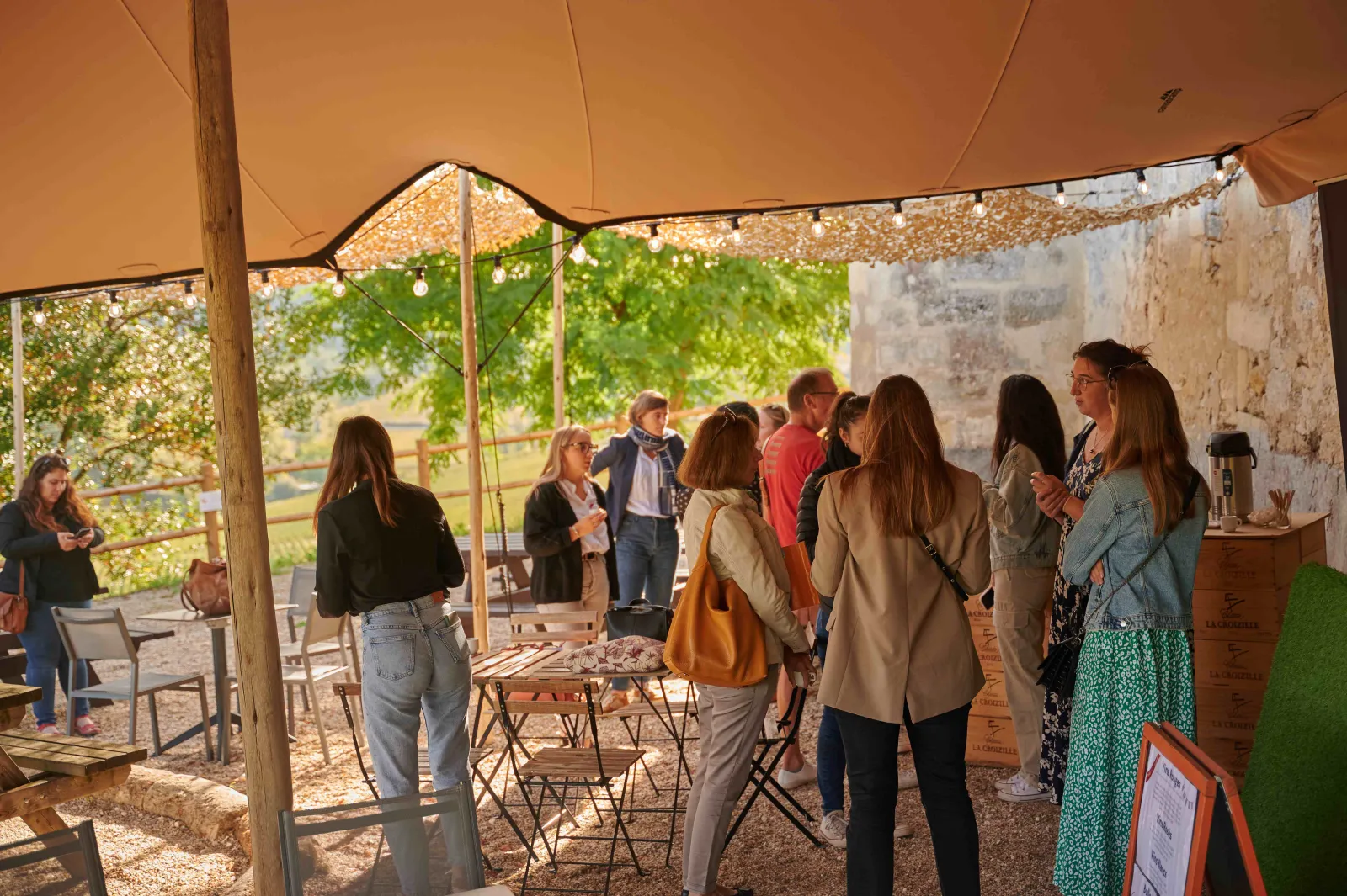 Visitors gathered under an orange tent in the courtyard of Château Tour Baladoz in Bordeaux, enjoying a wine tasting outdoor event.