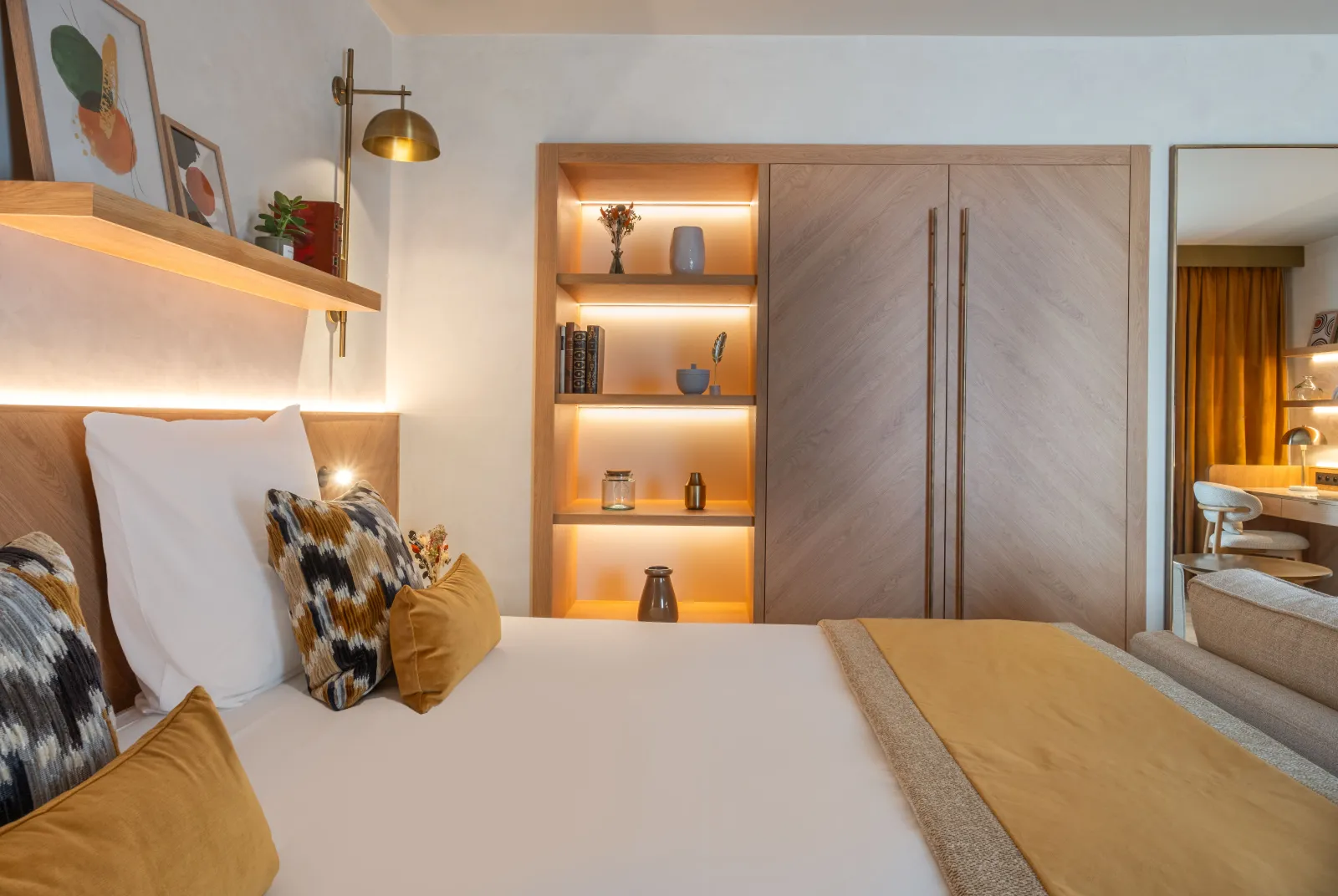 Elegant bedroom at Hotel Burdigala in Bordeaux featuring a white bed with yellow pillows, illuminated wooden shelving, light wood cabinetry, and contemporary décor
