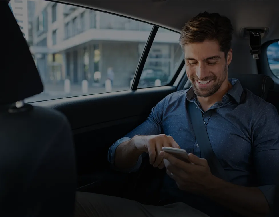 Smiling man using a smartphone in the back of a SIXT Ride vehicle in Bordeaux, with buildings visible in the background