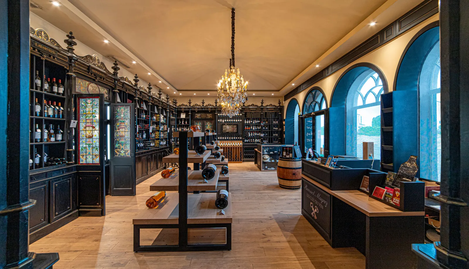 Elegant wine cellar interior with black cabinetry, bottle displays, golden chandelier, blue arches and wine exhibition tables at Château Pape Clément in Bordeaux