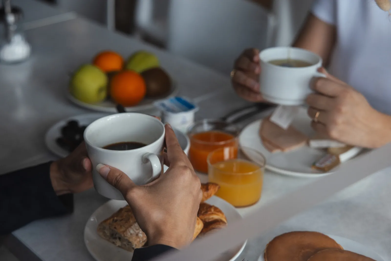Two people sharing breakfast at a table with coffee, toast, jam, and fresh fruits