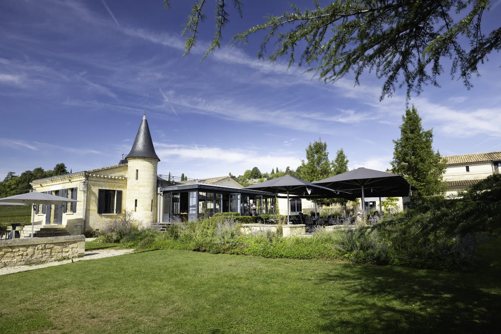 L'Atelier de Candale in Bordeaux, a modern architectural building featuring a conical tower, surrounded by lush gardens and shaded terraces.