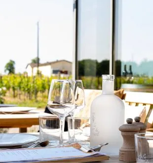 Wine tasting table at Chais de la Fleur in Bordeaux with empty wine glasses, white bottle, and vineyard landscape in the background
