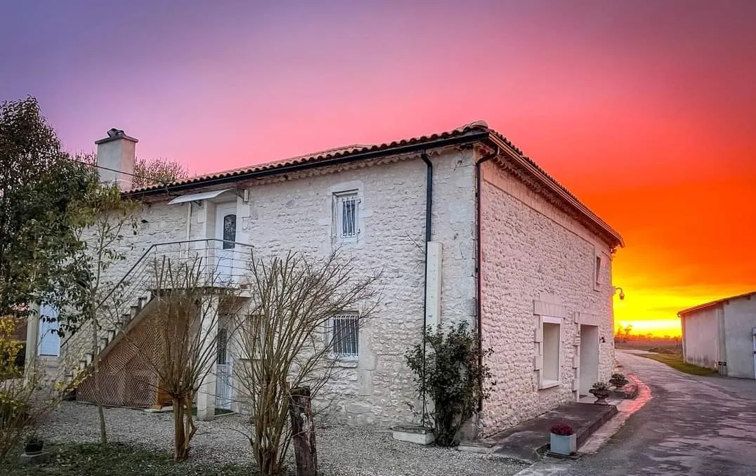 Pierre de Montignac Castle near Bordeaux, a white stone building with a tiled roof, photographed at sunset with a pink and orange sky.