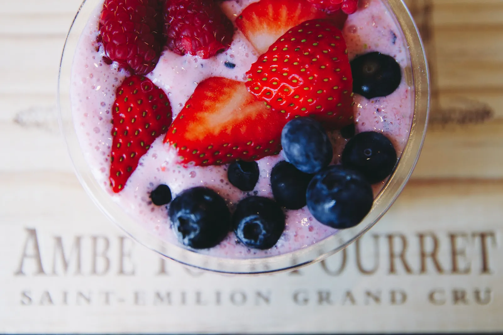 Glass of pink yogurt or mousse topped with sliced strawberries, raspberries and fresh blueberries, placed on a document mentioning Château Ambe Tour Pourret in Bordeaux