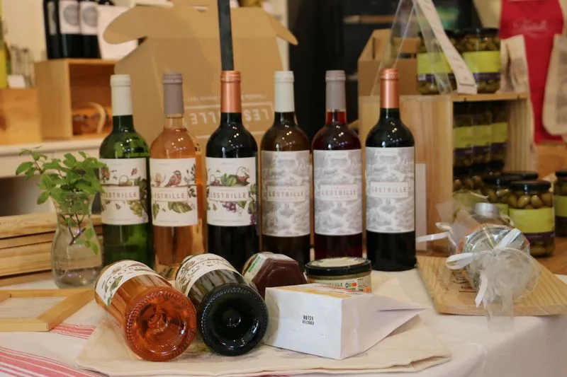 Wine display from Château Lestrille in Bordeaux featuring six upright bottles and two bottles lying down in the foreground, arranged on a tasting table with plants and accessories.