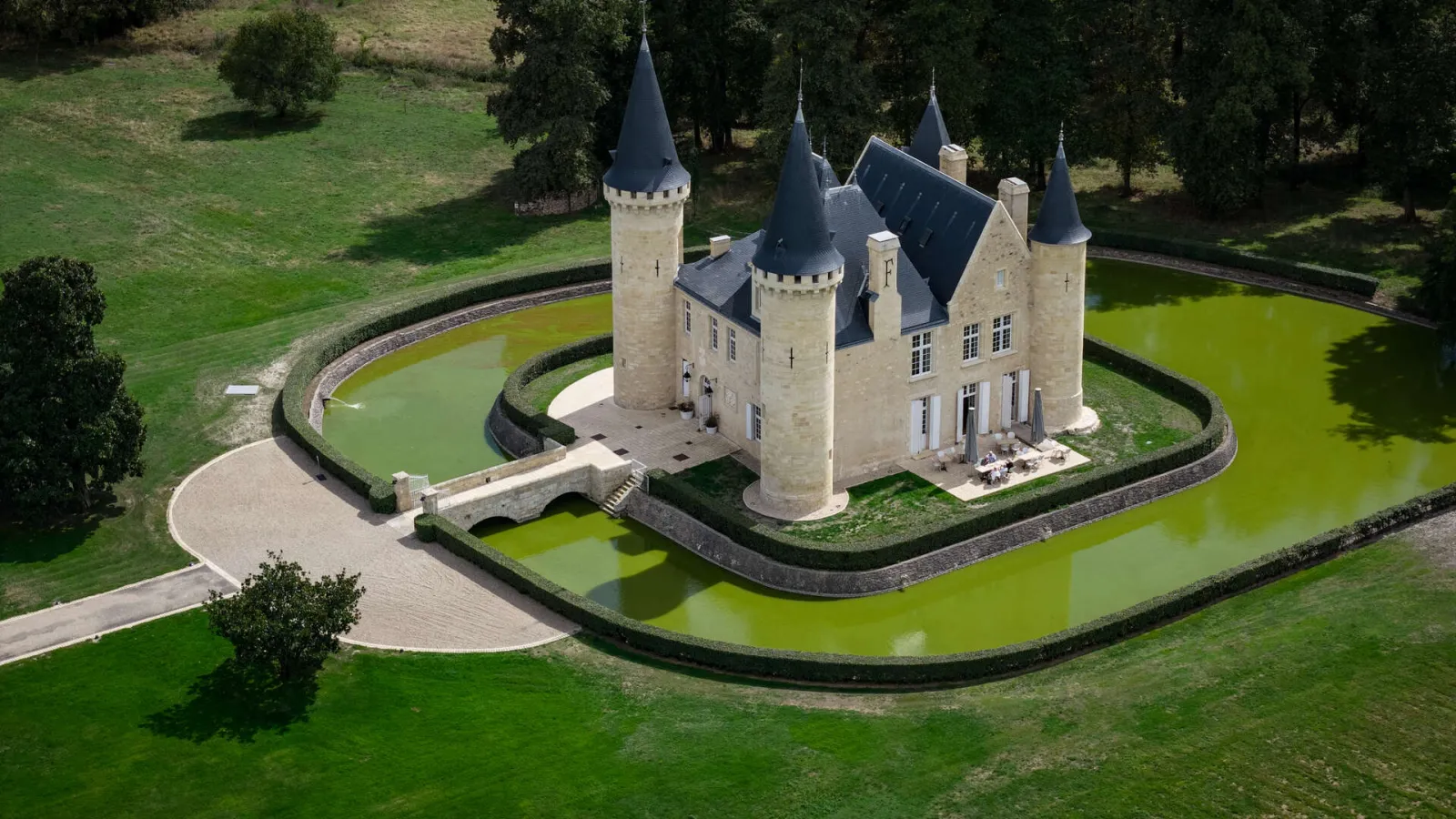 Aerial view of Château d'Agassac near Bordeaux, a medieval fortress with four conical towers surrounded by a water-filled moat, accessible via a stone bridge.