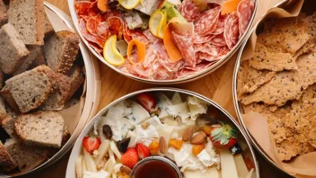 Charcuterie and cheese board with crackers and toasted bread, featuring sliced ham, cured meats, and white cheese with vegetables