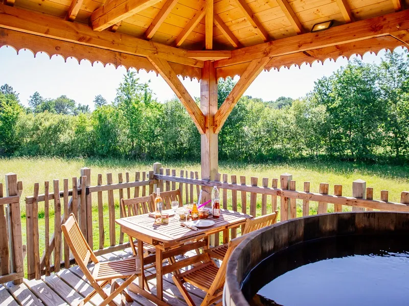 Wooden covered terrace with dining table, chairs and circular hot tub overlooking a green park at EcÔtelia Domain in Bordeaux
