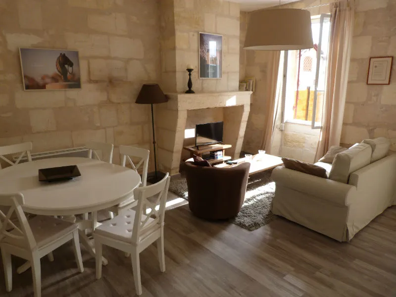 Elegant living room at the Maison des Hôtesses in Bordeaux featuring a white round table, matching chairs, beige sofa, brown armchair, stone fireplace and minimalist decor.