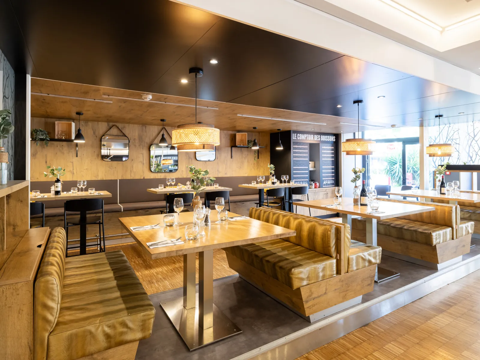 Contemporary dining room of Le Bistrot de Mériadeck in Bordeaux featuring wooden tables, golden booth seating, warm lighting, and natural wood wall panels.