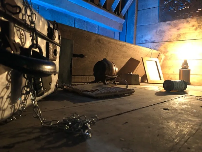 Interior of an escape room at Château de Lisennes in Bordeaux, featuring mysterious equipment including chains, a globe, metal objects, and dramatic yellow and blue lighting.