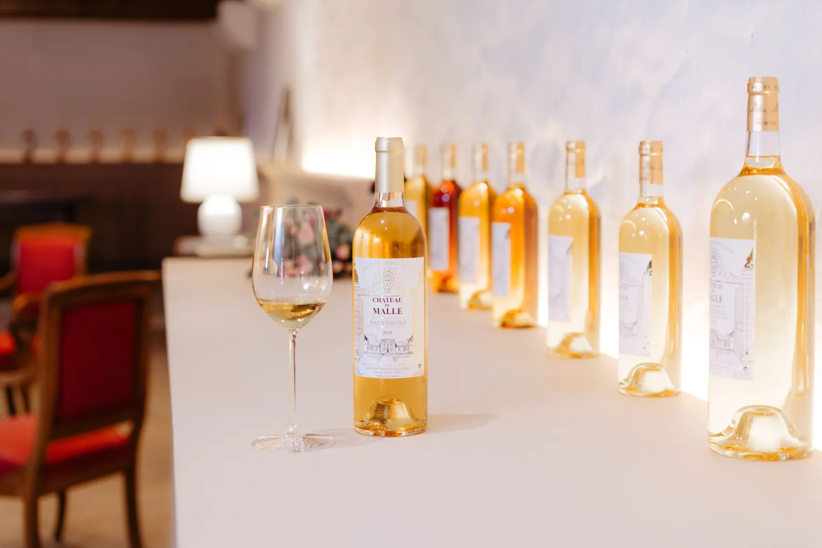 Wine tasting display of Château de Malle white wines in Bordeaux, featuring multiple bottles arranged on a white table with a filled glass in the foreground