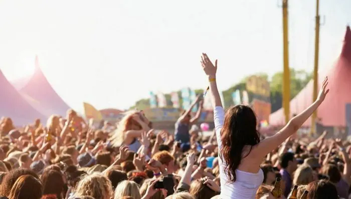 Crowd of spectators with raised arms enjoying an outdoor concert at Bordeaux's Music Festival, with pink tents and structures visible in the background.