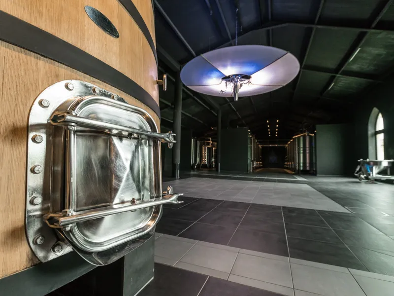 Modern interior of Château Malescasse in Bordeaux featuring a polished metal porthole window on a wooden wall, contemporary ceiling with blue lighting, and grey tiled flooring