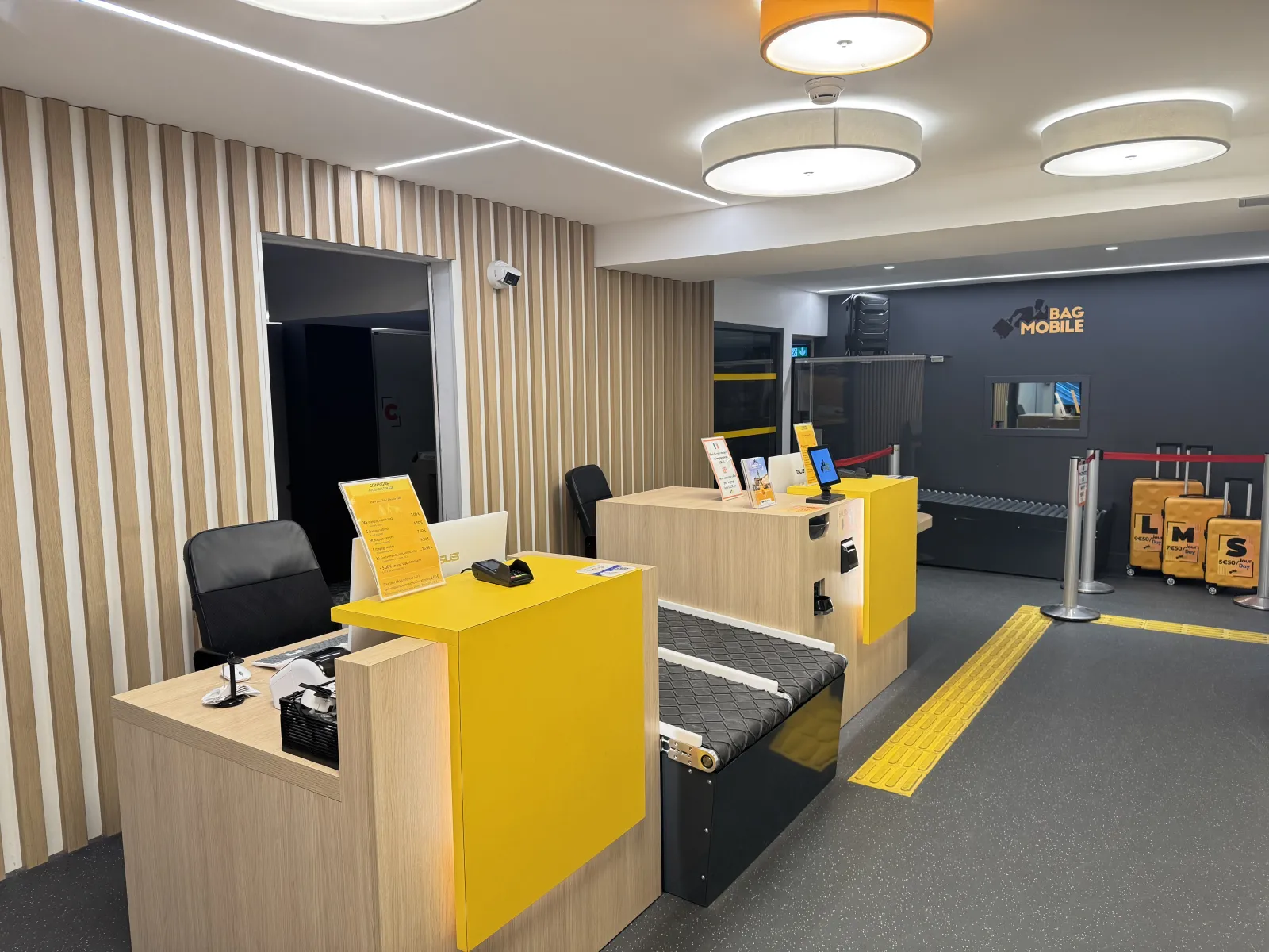Modern interior of a Bag Mobile store in Bordeaux featuring yellow and wooden counters, black chairs, contemporary lighting, and brand signage on dark gray wall