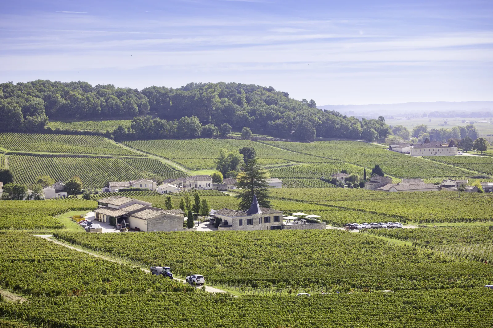 Aerial view of Château de Candale surrounded by Bordeaux vineyards, featuring its characteristic buildings, chapel, and wine production facilities scattered across rolling landscape.