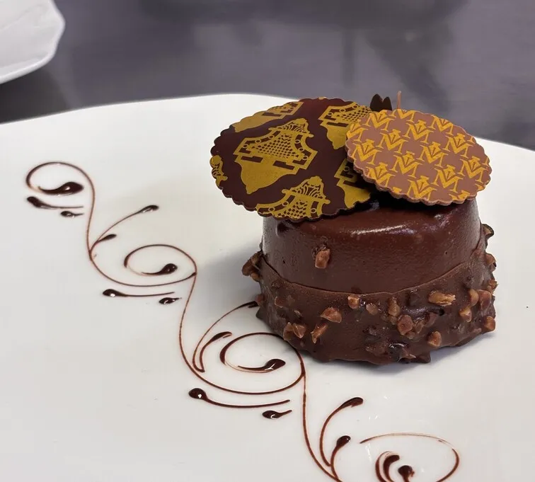 Chocolate dessert with glossy coating and gold leaf decoration on a white plate with chocolate flourishes, served at Le Cercle de Montaigne restaurant in Bordeaux