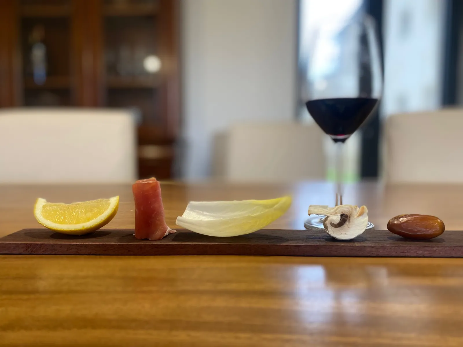 Gourmet food presentation featuring lemon, tomato, apple slice, mushroom and almond on a dark wooden board, paired with a glass of red wine in an elegant château setting