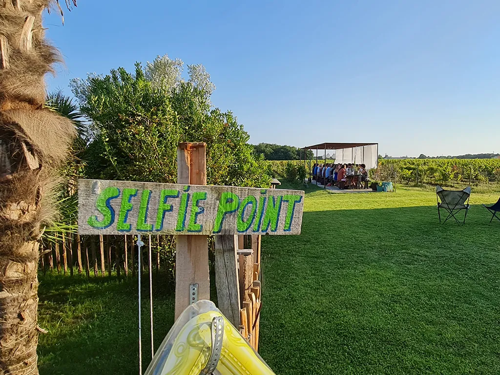 Green 'SELFIE POINT' sign in the vineyards of Château Hourtin-Ducasse near Bordeaux, with visitors in the background and a yellow kayak in the foreground