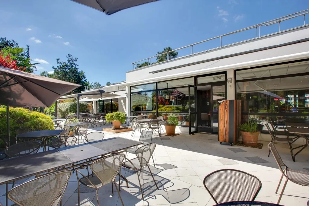 Sunny outdoor terrace of Hippopotamus restaurant in Bordeaux featuring metal tables and chairs, gray umbrellas, and a modern building with large glass windows