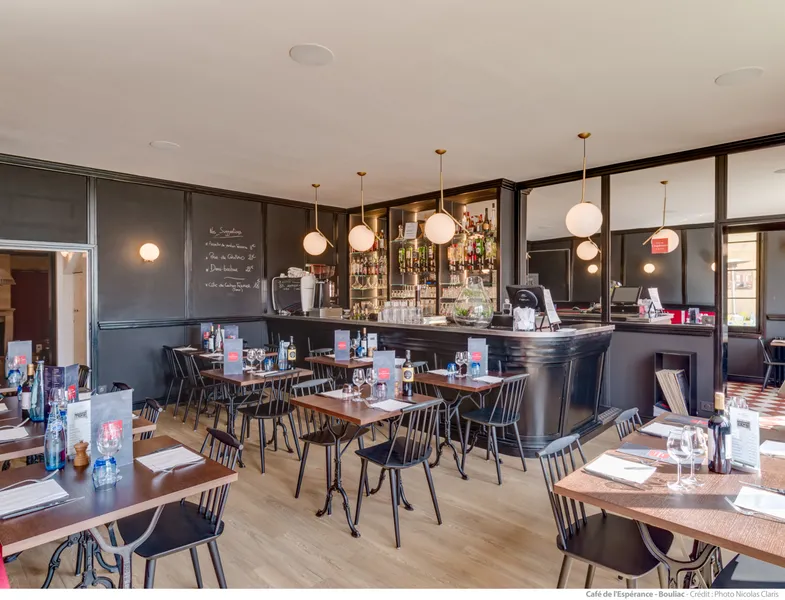 Interior of Café de l'Espérance in Bordeaux featuring wooden tables, black chairs, elegant bar counter, gold pendant lights, and sophisticated décor