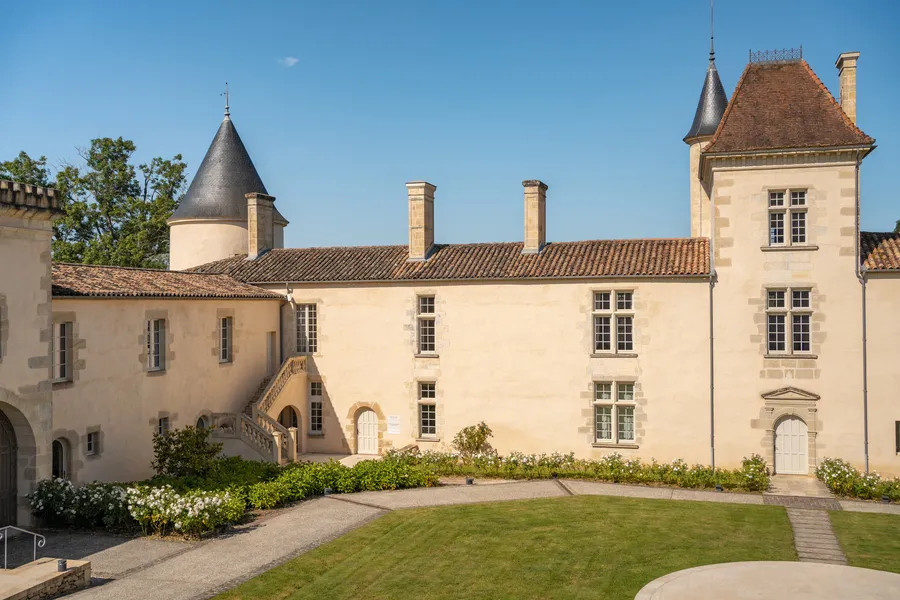 Façade of Château Toulouse-Lautrec in Bordeaux, a cream-colored stone building with two pointed towers, regularly spaced windows, tiled roof and inner courtyard with lawn.