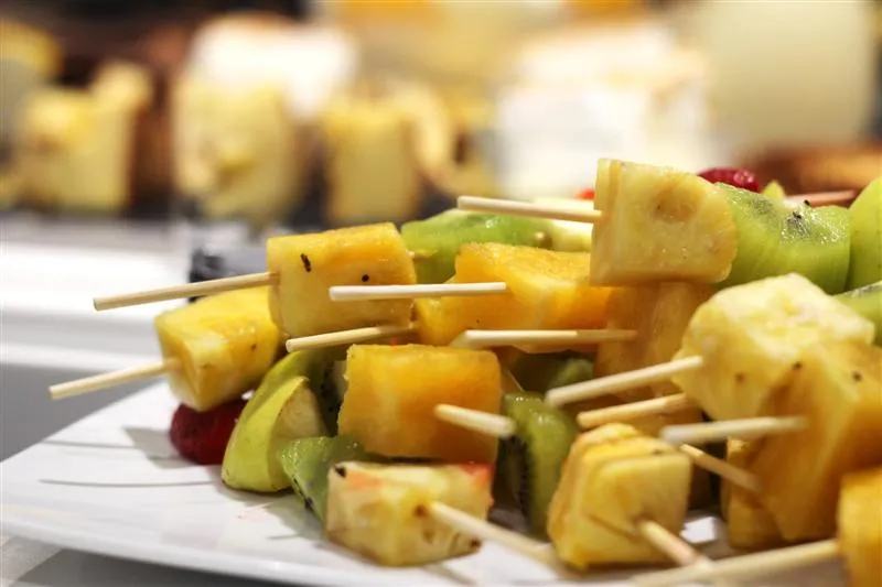 Grilled fruit skewers with pineapple, kiwi, and mango pieces on wooden sticks, arranged on a white plate