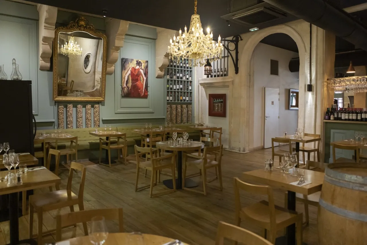 Elegant interior of Le Comptoir d'Etienne restaurant in Bordeaux featuring wooden tables and chairs, crystal chandelier, gilded mirror, wall paintings, and refined classical decoration.