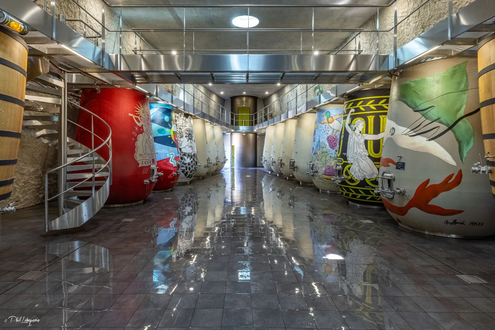 Underground cellar gallery at Château Les Carmes Haut-Brion in Bordeaux featuring decorated fermentation tanks with colorful street art, polished black marble floor, and modern concrete ceiling lighting.