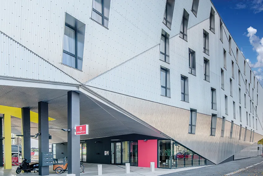Modern white facade of Appart City Confort Bordeaux Chartrons with contemporary architecture, covered entrance with gray columns, pink signage and retail access in Bordeaux