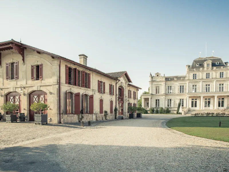 Courtyard of Château Giscours in Bordeaux featuring stone buildings with red shutters and the classical château facade in the background