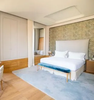 Elegant bedroom at Château de Ferrand in Bordeaux featuring a white bed, gold patterned wallpaper, light wooden wardrobe, pale blue carpet and bathroom access